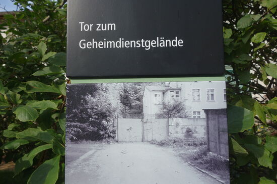 Das Foto zeigt ein Tor zwischen dem geschlossenen Geheimdienstareal und dem Wohngebiet am Kapellenberg, # das als offenes „Militärstädtchen" galt. Es wurde vor allem von Geheimdienstmitarbeitern genutzt. Nicht weit entfernt befand sich die Kreisdienststelle des Ministeriums für Staatssicherheit der DDR (MfS). Beide Dienste arbeiteten bei Observierungen und Verhaftungen eng zusammen.