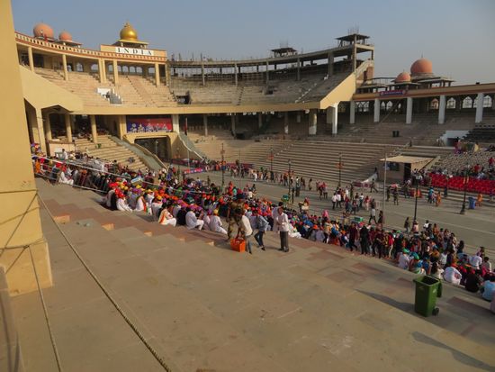 Wagah ist ein Grenzübergang an der Straße zwischen Amritsar, Punjab (Indien) und Lahore, Punjab (Pakistan). Es ist der einzige Grenzübergang in den genannten Bundesstaaten zwischen Indien und Pakistan. An der Grenze wird allabendlich auf beiden Seiten eine Militärparade der Grenzsoldaten abgehalten, die unter anderem die Flaggenparade und das Ertönen der Signaltrompete beinhaltet. Sie dient eigentlich der Demonstration militärischer Präsenz und Kampfbereitschaft. Die beiden Staaten haben - wir wir wissen - aufgrund historischer und aktueller anhaltender Feindseligkeiten ein eher angespanntes politisches Verhältnis.
Die Parade zeichnet sich allerdings dadurch aus, das auf beiden Seiten eine Stunde lang spiegelbildlich exakt das Gleiche !!! geschieht. Beim Einholen der Flaggen auf beiden Seiten wird peinlich genau darauf geachtet, daß keine tiefer hängt als die andere. Das Ganze erinnert stark an Monty Python.
