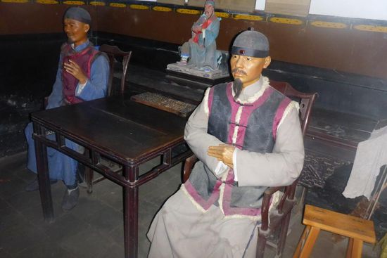 Nachgestellte historische Hausszene:
Der Hausherr sitzt rechts, der Besucher links,
Frauen halten sich in Nebenräumen auf