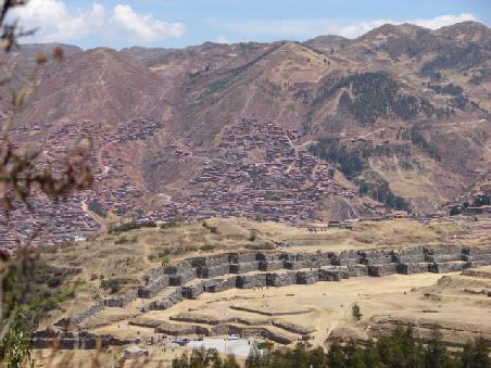 Die Zick-Zack-Mauern begrenzen die dazugehoerigen Terrassen. Im Hintergrund waechst Cusco die Haenge empor.