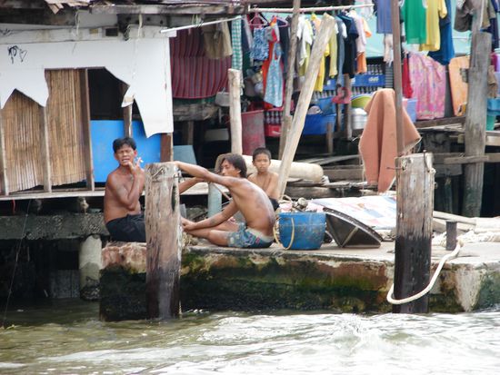 Blick vom Boot auf Thais vor ihren Wohnhaeusern.