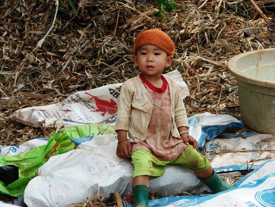 Nicht alle profitieren vom Tourismus: nur wenige Meter weiter muss der kleine Bub den Tag auf den Zementsaecken an der Baustelle verbringen, auf der seine Mutter fuer wenige Baht schuftet.