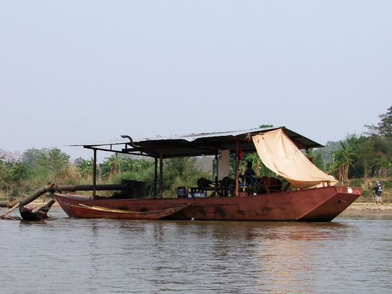 Mit altmodischen Schiffen und langen Rohrleitungen wird aus dem Flussbett Schotter gewonnen.