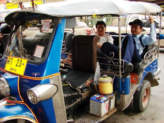 Fahrer samt Wachmann relaxen im Tuk Tuk, dem wichtigsten oeffentlichen Nahverkehrsmittel in Chiang Rai.