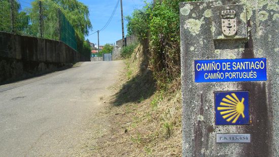 Ab hier beginnen die berühmten Meilensteine mit Jakobsmuschelkachel, die die Entfernung bis Santiago de Compostela anzeigen: von hier noch genau 115 Kilometer und 454 Meter!