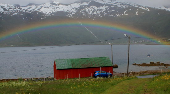 Frühstück, viel zu spät für den Tag, aber der Tag ist lang hier. 
Über dem türkisblauen Wasser erheben sich kahle Bergspitzen.
Zwischen den Wolken sieht man den neuen Schnee ganz oben. 
Im kleinen Haus sitzen wir ab Frühstückstisch. Wir schauen auf den Fjord, die Kaffeetasse in der Hand. Es ist ruhig im alten Haus. Nur nachts knarren die Dielen.
Ein einsamer Tümmler zieht seine Bahnen. Wir warten. Keine Hektik. Vielleicht kommt sie noch, die Sonne.
Da, ein Regenbogen!