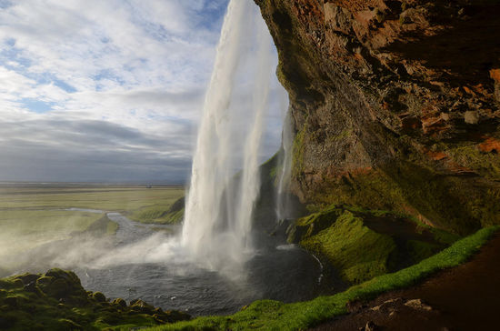 Um den Wasserfall herum führt ein schmaler, matschiger Rundweg durch die nasse Gischt hindurch zu einem geräumigen Hohlraum im Fels.