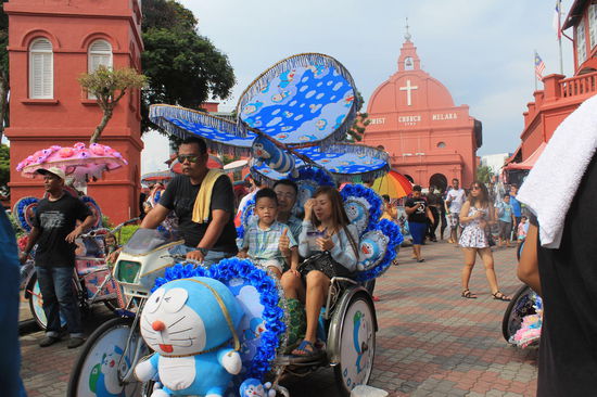 Beliebtestes Transportmittel fuer Touris in Melaka - die Topschlager sind im Frozen- und Hello Kitty-Design. Im Hintergrund der rote Platz in Melaka, die Gebaeude auf dem Platz sind von den Hollaender_innen gebaut wurden.