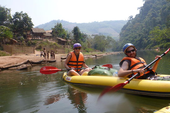Westler posieren vor laotischem Fischerdorf mit nackten, spielenden Kindern 