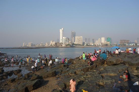 vorne Besucher des Haji Ali Dargah, dahinter etwas von der weit verzweigten Skyline Bombays