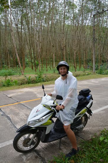 Mo im Regencape vor einer Kautschukplantage 