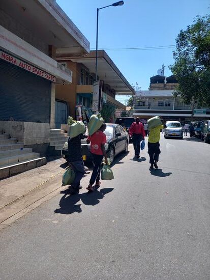Drei junge Männer tragen die Ware zum Auto. Sie erhalten dafür je 1000Tzs.