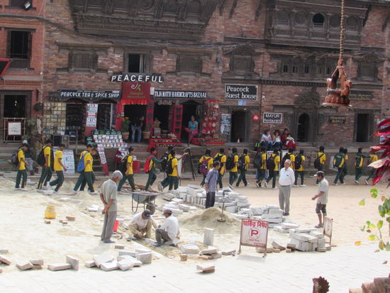 Auch hier werden die Schäden des Erdbebens behoben. Im Hintergrund unzählige nepalesische Schüler, brav hintereinander her.