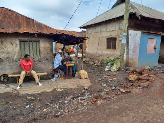 Gegenüber geht ein älterer Herr dem Schneiderhandwerk nach.