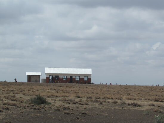 Nach einer Stunde Fahrt durch die Savanne taucht am Horizont die Schule auf. Schon von weitem sehen wir wie unzählige Kinder in die Schule strömen.