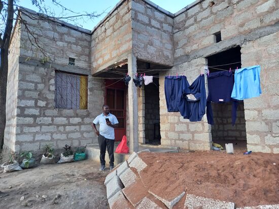 Dann erreichen wir das neue Zuhause der Familie. Sie haben sich seit meinem letzten Besuch ein kleines Grundstück gekauft und dieses Haus gebaut. Wir würden sagen, es ist ein Rohbau. Aber sie bewohnen bereits ein Zimmer. Fenster gibt es noch nicht. Daher ist die Fensteröffnung mit Plastik Plane verschlossen. Draußen hängt die Schuluniform von Aisha zum trocknen.