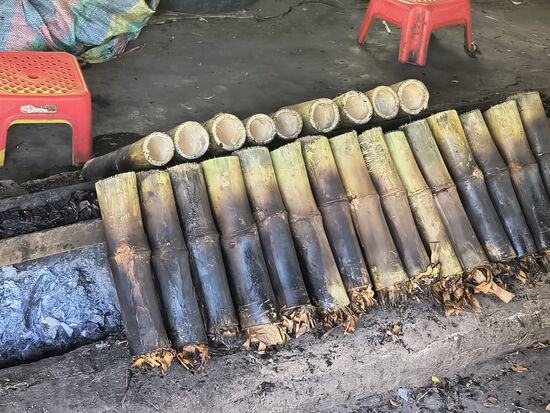 Für Sticky Rice werden Bambusstücke abgesägt, mit einer Mischung aus Reis, Kokosmilch, Zucker und schwarzen Bohnen gefüllt, mit Stopfen aus Bananenblättern versehen und über offenem Feuer gegart
