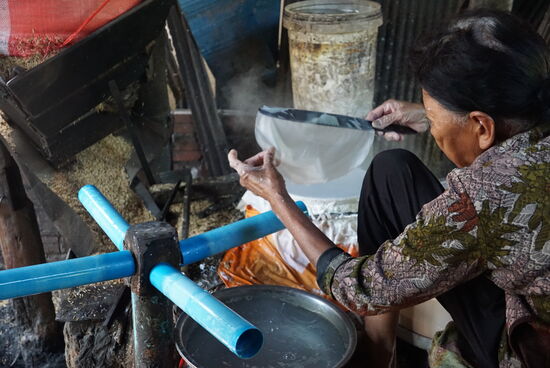Das frisch gebackene Reispapier ist noch nass und sehr empfindlich, es wird erst über die blauen Röhren gehängt  und mit diesen dann auf Drahtgeflecht abgerollt. Die ältere Dame sitzt den ganzen Tag vor ihren 2 Pfannen die mit Holz befeuert werden und backt das Papier aus einem sehr dünnen Teig aus Reismehl und Wasser