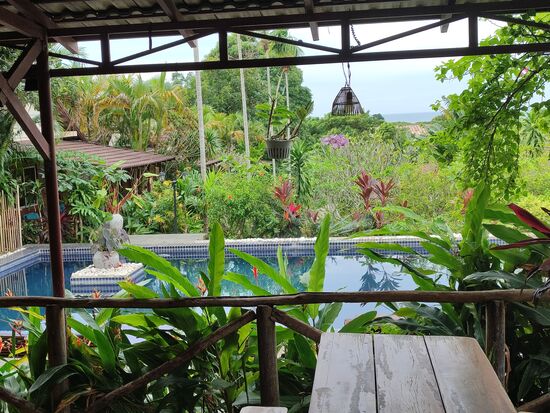 links sieht man ein Häuschen und vor dem Pool die große Terasse zum essen und sitzen