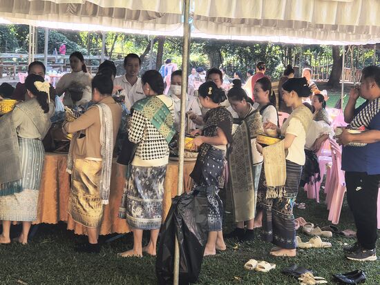 Spendenfeier an der Lagune, alle Gläubigen gehen an den Plastiktüten der Mönche vorbei und füllen sie mit Geld, Süssigkeiten und Crackern