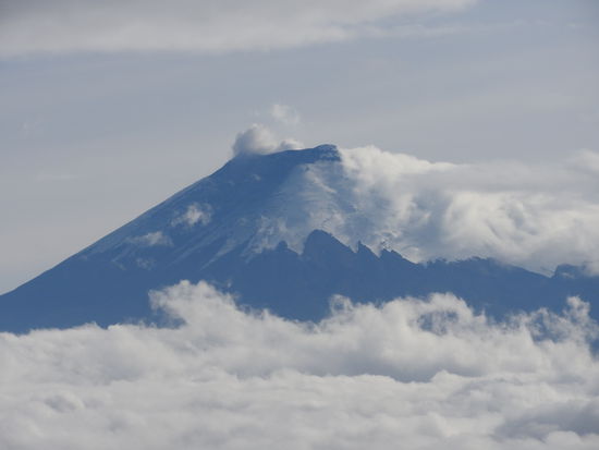 Der Gipfel des Cotopaxi schaut aus den Wolken. Rechts kann man die Eisfelder an der Südseite erkennen, die Nordseite ist fast eisfrei. Die Klimaveränderung lässt die Andengletscher immer schneller abschmelzen
Oben sind  rauchende Fumarole sichtbar