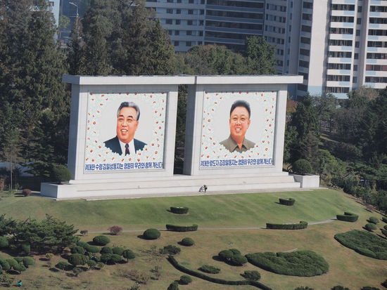 Eine einzelne Frau reinigt die Bilder von Kim Il-sung und Kim Jong-il