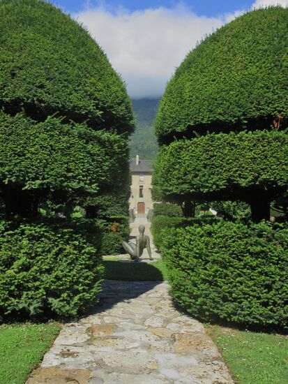 Eiben, Bronzeskulptur und im Hintergrund das Priorat