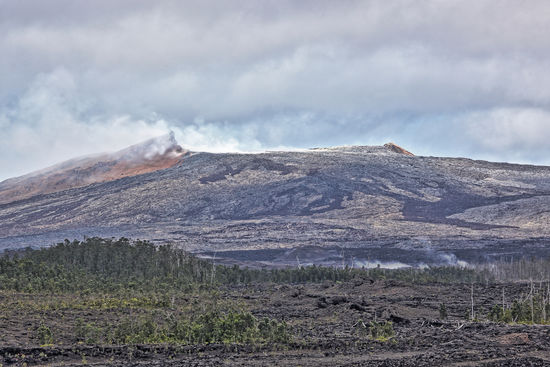 Rötliches Gestein ziert den Kraterrand, sonst sind die Farben der Abhänge des Pu'u O'o grau oder schwarz, je nach Alter der erkalteten Lavaströme. Näher als hier kommt man dem Pu‘u O‘o nicht. Es wäre ohnehin zu gefährlich. Es ist für uns faszinierend genug, dass wir die Quelle jahrzehntelanger vulkanischer Aktivität sehen dürfen. Ein Hubschauberrundflug wäre natürlich einfacher gewesen, aber es hat einen eigenen Reiz, sich solche Highlights im Urlaub hart zu erarbeiten. Die Eindrücke von der Wanderung sind natürlich auch nicht mit einem Hubschrauber-Quickie zu vergleichen.