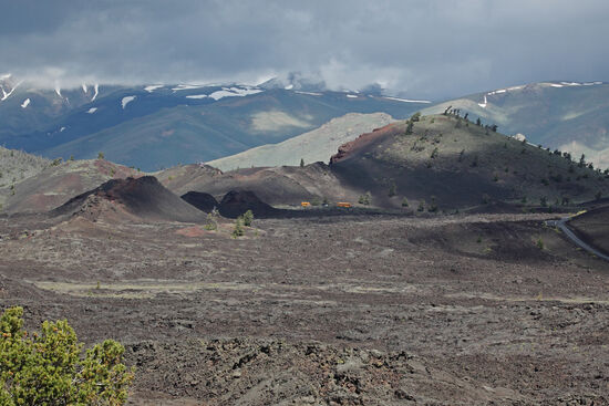 Schulausflug auf den Mond
Wer genau hinschaut, sieht zwei Schulbusse, die vor einer Ansammlung von Hornitos und grösseren Kratern im Craters of the Moon National Monument parken. Im Hintergrund sieht man die hier in die Snake-River-Ebene steil abfallenden Rocky Mountains.