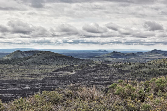 Craters of the Moon
Auch wenn jetzt im Frühling noch etwas Vegetation sichtbar ist, wird das Gelände des Craters of the Moon National Monument im Sommer zu einer schwarzbraunen Vorhölle. Lavafelder bis zum weit entfernten Horizont beherrschen das Bild. Mit knapp 2900qkm Grösse sind die Craters of the Moon um fast 20% grösser als das Saarland. Vor 11 Millionen Jahren befand sich der Yellowstone-Hotspot genau hier, aber die vielen schwarzen Lavaflüsse, die hier zu sehen sind, sind deutlich jüngeren Datums. Der Vulkanismus hier ist nicht erloschen, aber derzeit ruhend. Der letzte grosse Ausbruch hier fand vor etwa 2000 Jahren statt.