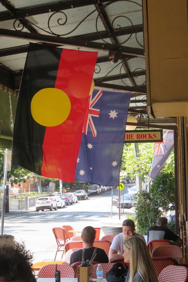Unter über uns die Fahne Australiens mit dem Union Jack, sechs Sternen für die sechs Bundesstaaten im blauen Ozean gelegen. Im Vordergrund die Fahne der Aboriginies