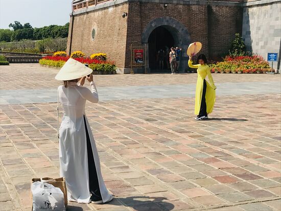 Junge vietnamesische Frauen in traditioneller Kleidung - lange und am Hals hochgeschlossene, aber an beiden Seiten bis zur Taille geschlitzte Kleider, zumeist aus Seide und in bunten Farben. Unter den Kleider tragen die Frauen weite Hosen.