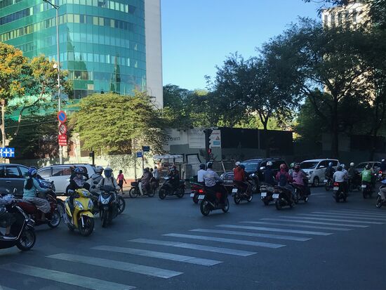 Berufsverkehr in der Saigoner Innenstadt. Mopeds bestimmen den Verkehr, Regeln scheint es nicht zu geben bzw. die Mopedfahrer bestimmen sie. Sie fahren überall. Wenn es auf den Straßen zu voll ist, dann brausen sie auch auf den Fußwegen vorbei. Einbahnstraßen wie Zebrastreifen werden regelmäßig ignoriert.