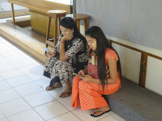 Junge Frauen in typischer bunter Kleidung und im Gesicht die Tha-na-ka Creme, die durch das Reiben der Rinde einer bestimmten Holzart gewonnen wird und als Schutz vor der Sonne, aber auch als Schönheitscreme im Gesicht aufgetragen wird. Selbst Kinder und auch Männer tragen die Creme auf.