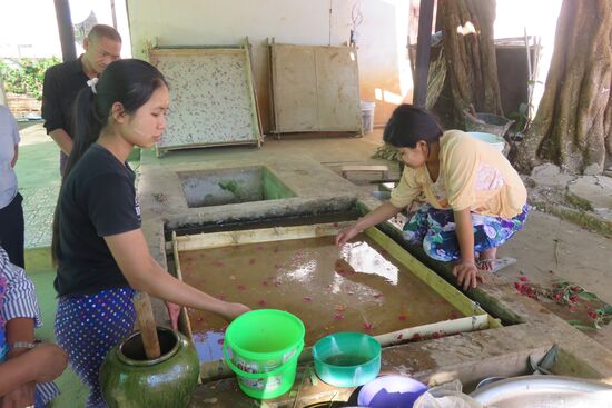 Der Rindenbrei wird  in  viereckige  Siebrahmen eingeschwemmt, dann hochgezogen und mit Blüten versehen. .