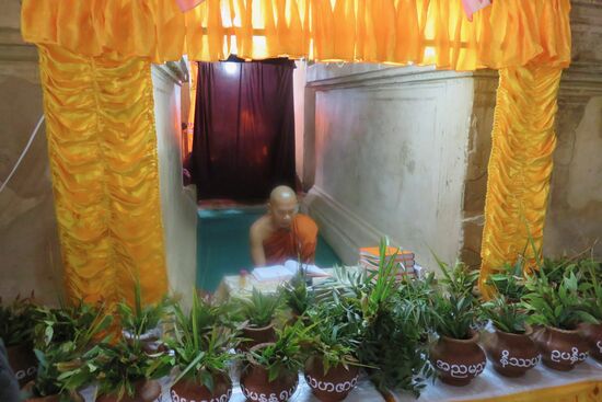 Während ein Mönch laut mit Mikrofon betet, warten seine "Kollegen" auf ihre Schicht hinter dem roten Vorhang.