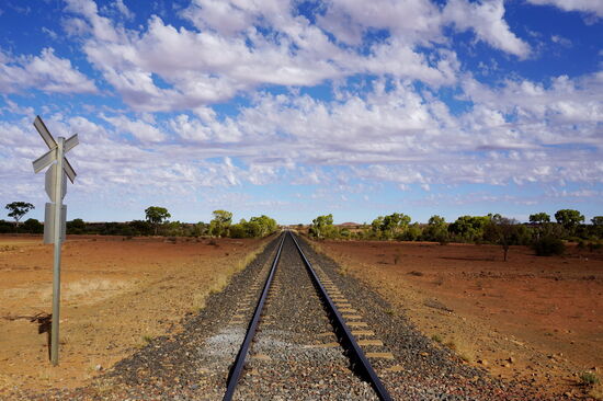 
Kurze Geschichte der Ghan-Bahn und der zugehörigen Service-Piste: es wurde Ende des 19. Jahrhunderts in South Australia von Port Augusta bis Marree zunächst eine Telegraphen-Leitung gelegt und dann hier entlang schließlich die frühere Eisenbahnstrecke „The Ghan“, heute OLD GHAN genannt, bis Alice Springs errichtet, wobei 1891 von Süden her Oodnadatta und 1929 Alice Springs erreicht wurde. Später wurde eine neue Strecke, die aber etwas weiter westlich verläuft errichtet. Sie wird auch The Ghan genannt und führt jetzt von Adelaide bis Darwin in 48 Stunden (Zwischenstopp in Alice Springs 4 Stunden). Die alte Bahnstrecke wurde abgerissen.
Später lesen wir:
Mit dem legendären Ghan durch Australien zu fahren, ist ein Erlebnis der ganz besonderen Art. Von Adelaide nach Darwin rollt der über 400 Meter lange Zug einmal pro Woche - in der Hauptsaison sogar zweimal wöchentlich. Beim Durchqueren des 5. Kontinents von Süd nach Nord passiert er 22,5 Breitengrade und 4 Klimazonen. Die Streckenlänge beträgt 2.979 Kilometer, für die der Fernverkehrszug 48 Stunden (zwei Tage und Nächte) benötigt. Die Route unterteilt sich in drei Hauptabschnitte:
1. Adelaide - Alice Springs (1.559 Kilometer),
2. Alice Springs - Katherine (1.108 Kilometer),
3. Katherine - Darwin (312 Kilometer).
