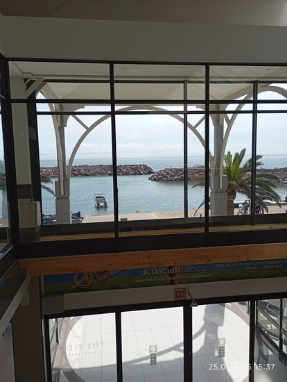 Blick aus dem Mittelgang des Einkaufszentrums durch ein selbsttätiges Schiebe-Glastor auf den Hafen. Doch selten öffenen Kunden das Tor, es kommt dann ein kühler Luftstoß entgegen.