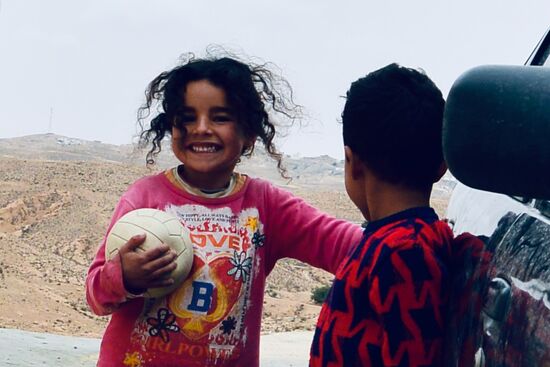 zwei Kinder mit pechschwarzen Zottelhaaren toben mit scheinbar endloser Energie um ein altes Auto herum