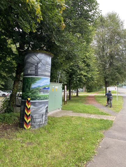 Hier wird ganz offen mit der ehemaligen Teilung Deutschlands umgegangen. Ich finde es sehr gut, dass daran erinnert wird. Die DDR hat ihre Bürger eingesperrt und dafür massive Zäune und Grenzschutzanlagen errichtet.
P.S.: Der Grenzpfahl ist nur aufgemalt. Von weitem glaubt man, der Pfahl ist echt.