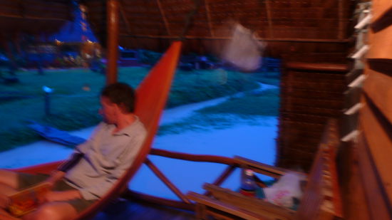 Martin in der Haengematte auf unserer Veranda... Das Wasser im Hintergrund sollte nicht sein, sondern kam, weil es stundenlang geregnet hatte. Wir waren sozusagen eingeschlossen... oder mussten durch 30cm tiefes Wasser zur Bar latschen. Heute Morgen war dann alles wieder trocken und nur noch leicht Matschig.. (kennt man ja von den OpenAirs )