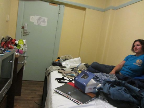 Wir beim Versuch in einem 5m²-Zimmer zu packen. In dieser Zelle hat man es dennoch geschafft 1 Bett, 1 Waschbecken, 1 Heizkörper, 1 Kühlschrank, 1 Fernseher, 1 Standventilator und ein Regal unterzubringen.