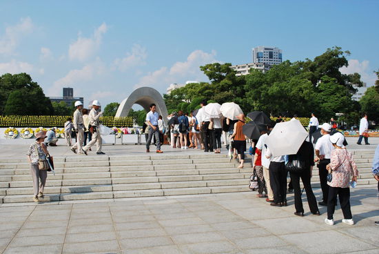 Viele Menschen legen Blumen nieder an dieser Stelle und stehen dafür in der brütenden Hitze Schlange