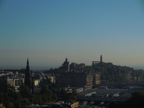 Blick von der Burg über Edinburgh: Die 3 landmarks, die hier in die Höhe ragen sind von vorne nach hinten das Scott Monument, der Uhrturm des Balmoral Hotels und das Nelson Monument auf dem Calton Hill. Das große Dach im Vordergrund gehört zum Bahnhof Waverley Station.