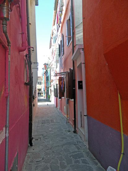 Burano - Durch enge Gassen führt uns der Weg. Witzig, manchmal stehen 
Schuhe oder Pantoffeln auf den Fensterbänken draußen an den Häusern. Auch Besen und andere Reinigungsgeräte baumeln draußen an den Häusern.