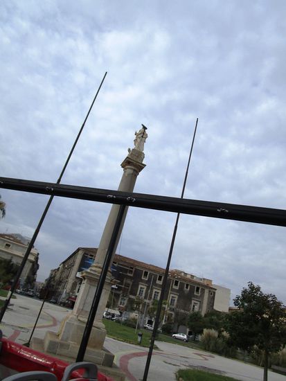 Zum Glück erwische ich die Statue der Heiligen Agatha auf der Piazza Martiri della Liberta. 
Die Statue der Heiligen Agatha, errichtet auf einer römischen Säule des Amphitheaters, erinnert an das Wunder von 1775 als die Heilige die Stadt vor der Pest bewahrte.
Auf dem Platz wurden 8 Revolutionäre erschossen, die sich gegen das Regime erhoben hatten – Märtyrer der Heimat für die Freiheit.
Die Piazza erhebt sich über der alten Lava del Larmisi, hier soll sich ein heidnischer Tempel, der der Ar-temis geweiht war, befunden haben.