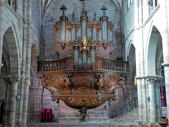 Die Orgelempore wird von einem kauernden Atlanten gestützt. Die darüber liegende riesige geschnitzte Holzkonsole wird von 4 Atlanten gehalten. Alles aus einem einzigen Stück Eiche geschnitzt.