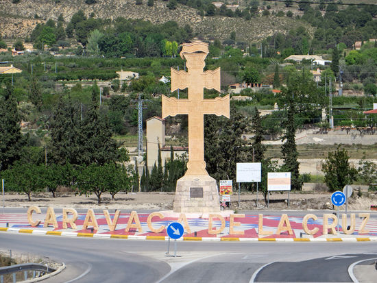 Verehrt wird das Kreuz von Caravaca, das in der Basilika über der Stadt aufbewahrt wird, die auch das Stadtbild beherrscht.
Zu verdanken hat Caravaca diese Gunst einem Splitter des Kreuzes Christi, der dem Ort auch zu seinem Beinamen “de la Cruz” verhalf und 1231, wohl durch einen Bischof von Jerusalem nach Caravaca gebracht wurde.
Die Legende erzählt aber folgende Geschichte:
Um 1231 soll in der maurischen Stadt Caravaca ein christlicher Priester den dortigen muslimischen Herrscher zum Christentum bekehrt haben, unter Mitwirkung eines Kreuzes, das von Engeln durch ein Fenster auf den Altar gebracht worden sein soll.
Caravaca-Kreuz ist die Bezeichnung für eine bestimmte Art von Kreuzen. Die Bezeichnung leitet sich ab vom Kreuz in Carava-ca de la Cruz in Spanien. Diesem werden wundertätige Kräfte zugeschrieben. Ein Caravaca-Kreuz hat zwei Querbalken, manchmal mit zwei Engeln unter dem unteren Balken. Im Kreuz befanden sich häufig Reliquien.
Seit dem 16./17. Jahrhundert verbreiteten sich Kreuze in der Form von Caravaca erst in Spanien, danach auch in anderen Teilen Europas. In Polen wurde das Kreuz seit dem späten 18. Jahrhundert populär, als Hilfe gegen Krankheiten und Epidemien wie die Cholera. Aber die Kreuze dienten auch für okkulte Zeremonien.