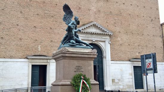 Das Denkmal der Gefallenen vor der Kirche
Ein beflügelter Sieg, der einen Kriegsgefallenen stützt, ist ein Werk von Domenico Trentacoste. Die zwei bronzenen Statuen stehen auf einem Sockel aus rotem Granit, auf welchem man eine Gedenkschrift, über die Gefallenen des ersten Weltkrieges findet.