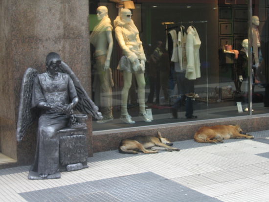 es gibt in den strassen viele unglaublich gute "move for money" kuenstler, die minutenlang regungslos sitzen und sich erst bewegen, wenn man geld ins kaesschen wirft. dieser hier wurde von den meisten menschen ueberhaupt nicht als person wahrgenommen - ein mann ist ihm mit seinem trolley sogar ueber die fuesse gefahren, da er vermutlich dachte es ist wirklich eine statue. 
die beiden hunde rechts dagegen sind keine kuenstler - sie lassen sich auch durch geld nicht zu einer bewegung hinreissen